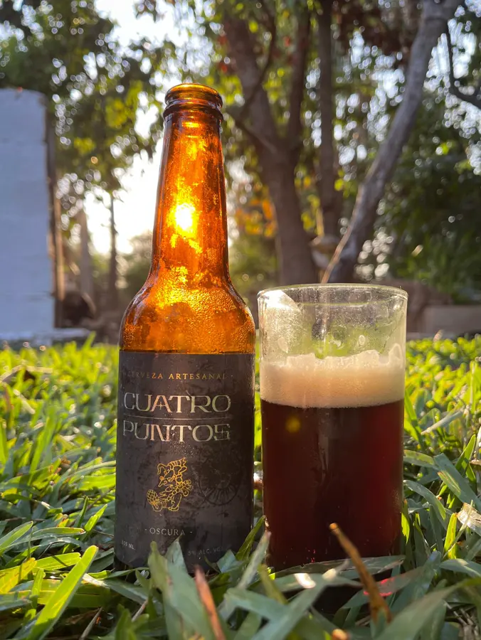 Botella ámbar al atardecer junto a un vaso de cerveza oscura